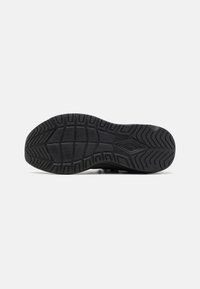 Semelle de sneaker noire avec une surface en caoutchouc texturé, des profondes nervures et un motif géométrique pour une adhérence et une traction améliorées.