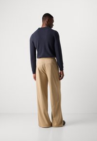 Suéter azul oscuro con un corte relajado y un cuello doblado, combinado con pantalones de pierna ancha en beige claro que cuentan con dos bolsillos traseros.