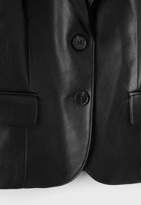 Veste en cuir noire à l'avant avec deux grands boutons ronds et deux poches à rabat à la taille, montrant un matériau à texture lisse.