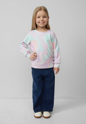 Pastelowy sweter tie-dye z napisem "MARZENIA SIĘ SPEŁNIAJĄ", w połączeniu z luźnymi ciemnoniebieskimi dżinsami i białymi butami, na szarym tle.