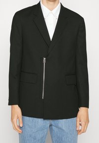 Schwarze Blazer mit einem einzelnen Reißverschluss, zwei Fronttaschen und taillierter Passform. Baumwollmischgewebe mit glatter Textur.
