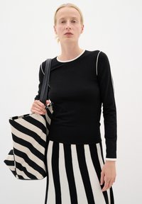 Melna garā piedurkne topiņa ar baltu apakšmalu, kopā ar melnu un krēmkrāsas svītrotu somu un svītrotu svārku, izceļot kontrastējošus rakstus.