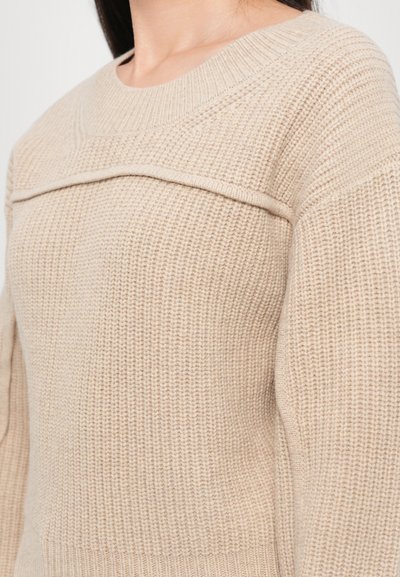 Maglione beige con un design a maglia testurizzata, caratterizzato da un collo rotondo e dettagli di striscia orizzontale sul petto. Tessuto morbido e caldo.