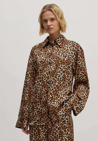 Leopardprint shirt in een glanzende stof; heeft een puntige kraag, lange mouwen en een relaxte pasvorm met variaties van bruin, zwart en crème.