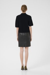 Fekete kötött, rövid ujjú felső, amelyet egy testhez álló fekete bőr szoknyával párosítottak. A modellen olívazöld magassarkú cipő van. Sima textúra, minimalista design.