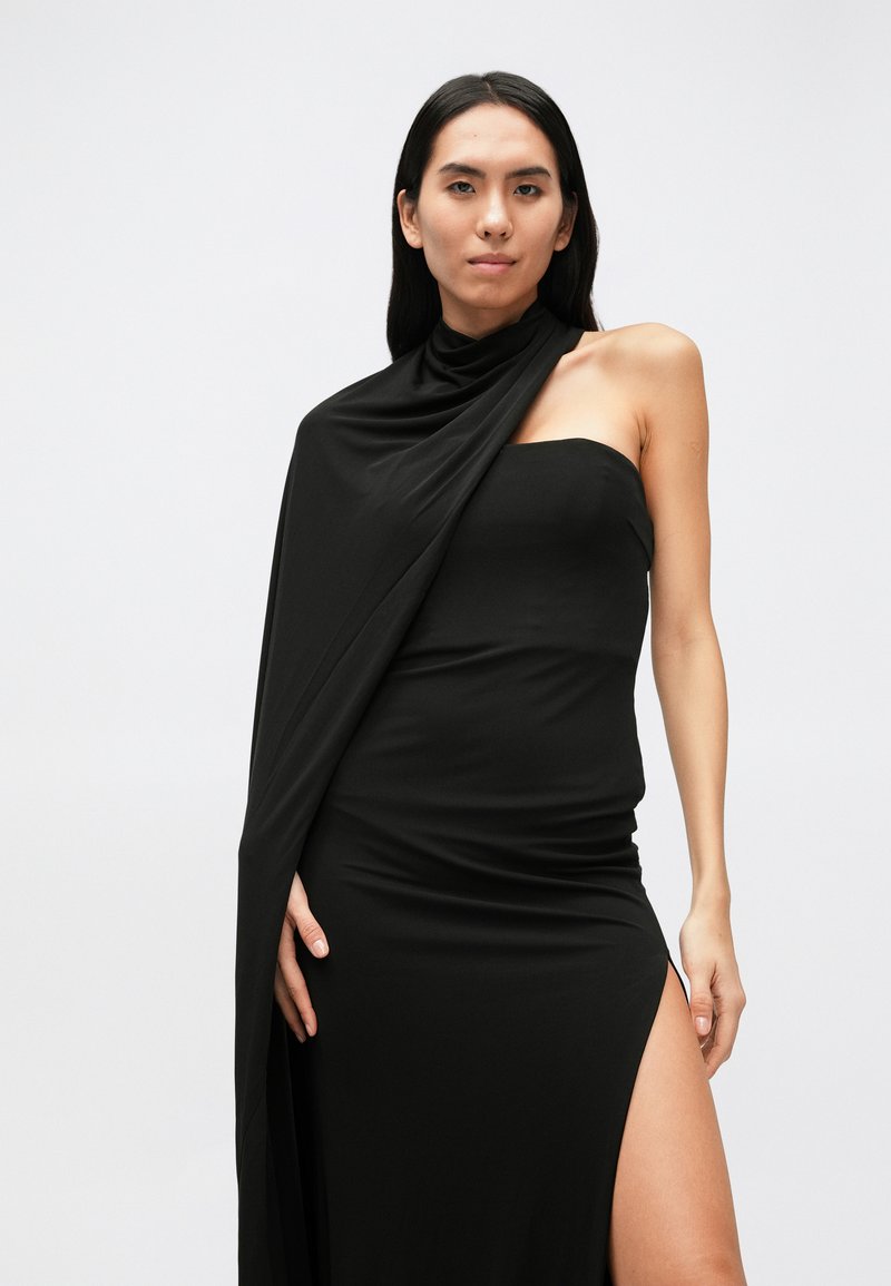 Black fitted dress with asymmetrical neckline, one shoulder draped fabric, waist slit, and smooth texture. Minimalist design, full length.