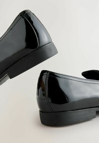 Schwarze Lackloafers mit elegantem Design, abgerundeter Spitze und niedrigem Gummihacken. Glatte Oberfläche mit sichtbaren Nähten und minimalen Akzenten.