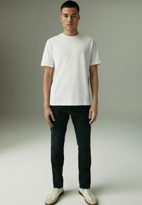 Witte t-shirt met korte mouwen, gecombineerd met zwarte broeken en lichtgekleurde sneakers. Eenvoudig ontwerp met een ontspannen pasvorm. Neutrale achtergrond.