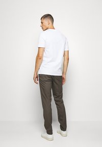 Hvid bomulds t-shirt parret med brune ternede bukser. Slim fit design med korte ærmer, set bagfra, og hvide sneakers.