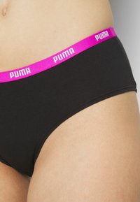 Crne gaćice s širokim fuksija elastičnim pojasom na kojem se nalazi bijeli logo "PUMA." Glatka tekstura, nisko strukirane i prilagođenog dizajna.