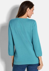 Türkiser Pullover mit strukturiertem Punktmuster, 3/4-Ärmeln und geripptem Saum. Der Rücken ist schlicht und betont die kräftige Farbe.