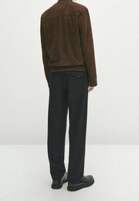 Bruine suède jas met een achterpas, gecombineerd met losse zwarte broek en donkere schoenen, met een achterzakdetail.