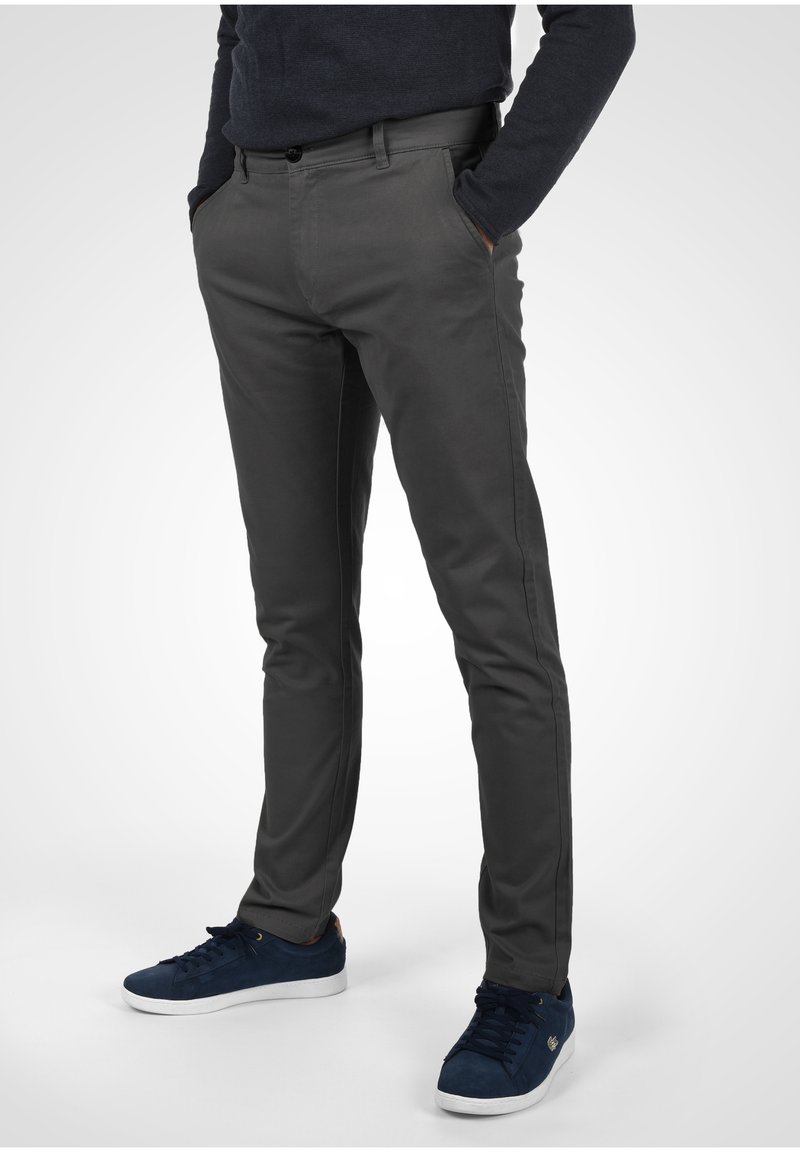 Pantaloni in cotone grigi con una vestibilità slim, evidenziati da tasche frontali e cuciture laterali sottili, abbinati a sneakers blu navy.