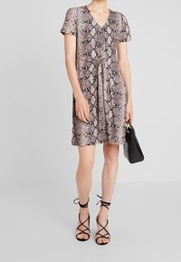 Robe à manches courtes avec un motif imprimé serpent, dotée d'un décolleté en V, d'une taille cintrée et d'une coupe décontractée. Associée à des talons noirs à brides et à un sac à main.