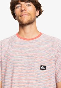 Striped t-shirt with a light fabric, featuring horizontal lines in coral and blue shades, a round neckline, and a left chest pocket with a logo.