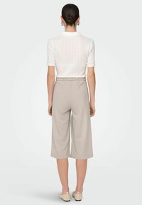 Biała prążkowana bluzka z krótkim rękawem w połączeniu z beżowymi spodniami o szerokich nogawkach i kroju 3/4. Miękki materiał z elastyczną talią i minimalistycznym designem.