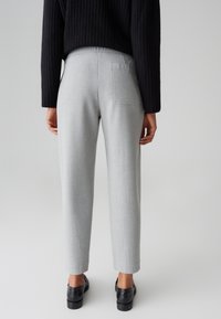 Graue maßgeschneiderte Hose mit geradem Schnitt, einer einzelnen Gesäßtasche und glatter Textur, kombiniert mit schwarzen Schuhen und einem dunkel gerippten Pullover.