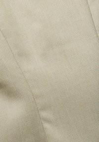 Gros plan d'un tissu beige avec un tissage fin et texturé et une couture visible traversant la surface en diagonale.