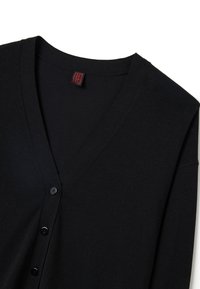 Schwarze Strickjacke mit V-Ausschnitt, langen Ärmeln, fünf schwarzen Knöpfen und einem roten Etikett im Kragen. Glatte, gestrickte Textur.