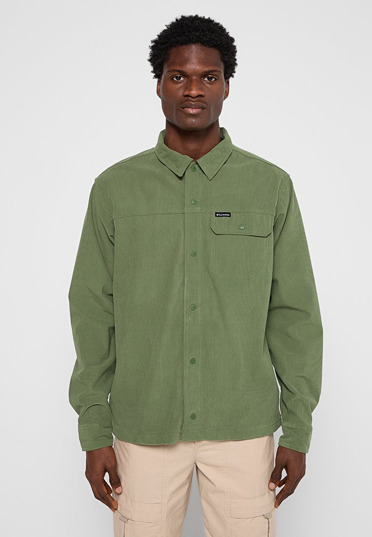 Zielona koszula z kordurowego materiału z zapięciem na guziki, długimi rękawami i jedną kieszenią na piersi. Posiada subtelną fakturę i wzór kołnierzyka.