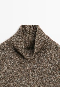 Hnědý pletený svetr s vysokým límcem a ribbovanou strukturou, který obsahuje různobarevné nitě v krémové, šedé a hnědé barvě. Viditelný silný zvýšený límec.