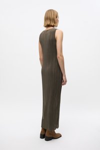 Langes, ärmelloses Kleid in olivgrün mit strukturiertem, plissiertem Stoff. Das Design hat einen hohen Halsausschnitt und seitliche Schlitze, kombiniert mit braunen Stiefeletten.