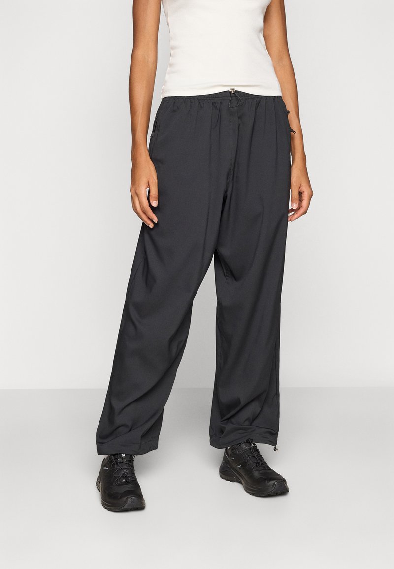 Schwarze, locker sitzende Hosen mit einem elastischen Bund und Reißverschlüssen an den Knöcheln, hergestellt aus einem glatten, leichten Material.
