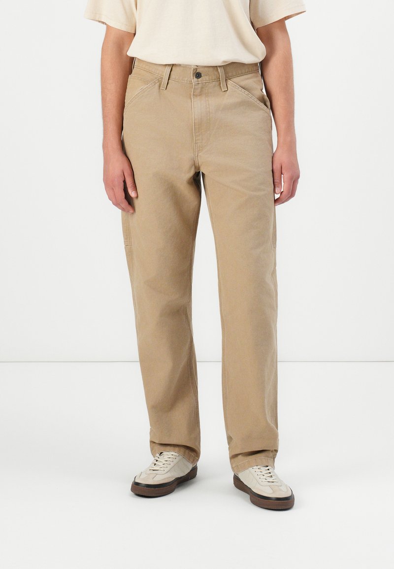 Beige cotton trousers with a straight-leg design, featuring two front pockets and a button closure. Worn with light-colored sneakers.