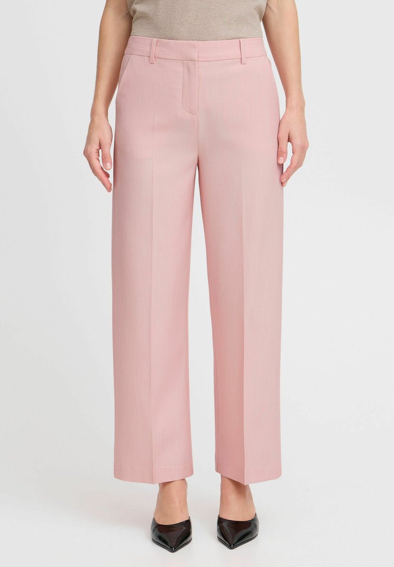 Pink wide-leg trousers made of smooth fabric. Features a tailored fit, front pockets, and a creased style. Worn with black pointed-toe heels.