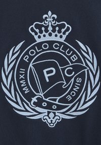 Il tessuto blu navy presenta un logo ricamato di colore azzurro chiaro con una corona, una corona di alloro, una bandiera e il testo "POLO CLUB" e "DAL MMXII."