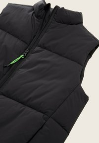 Zwarte gewatteerde vest met een voorrits en een felgroene trekband, hoge kraag en doorstikte delen voor isolatie.