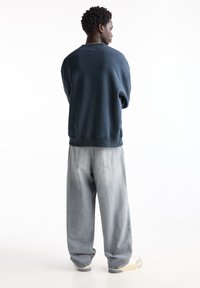Námornícky oversized mikina s klesnutými ramenami v kombinácii so svetlosivými širokými nohavicami. Oblečenie dopĺňajú biele tenisky s off-white akcentmi.