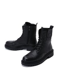 Botas de cuero negro con un acabado texturizado, cordones en la parte delantera, cremallera lateral y suelas gruesas con tacos. Presentan una cinta de agarre y un acento a presión.
