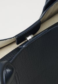 Sac à main en cuir bleu marine avec surface texturée, fermeture magnétique et doublure en coton. Présente des détails de couture contrastants le long des bords.