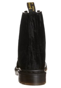 Černé semišové kotníkové boty s hladkou texturou, kulatou špičkou a gumovou podrážkou. Mají kontrastní žlutý poutko vzadu.
