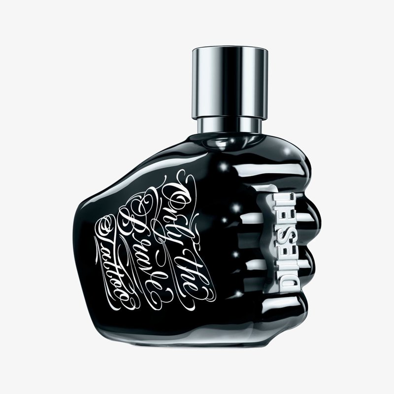 Musta lasipullo, joka on muotoiltu nyrkiksi kiiltävän hopean kannen kanssa. Pullossa on valkoisella scriptillä teksti "Only the Brave Tattoo" ja kohokuviointi "DIESEL."