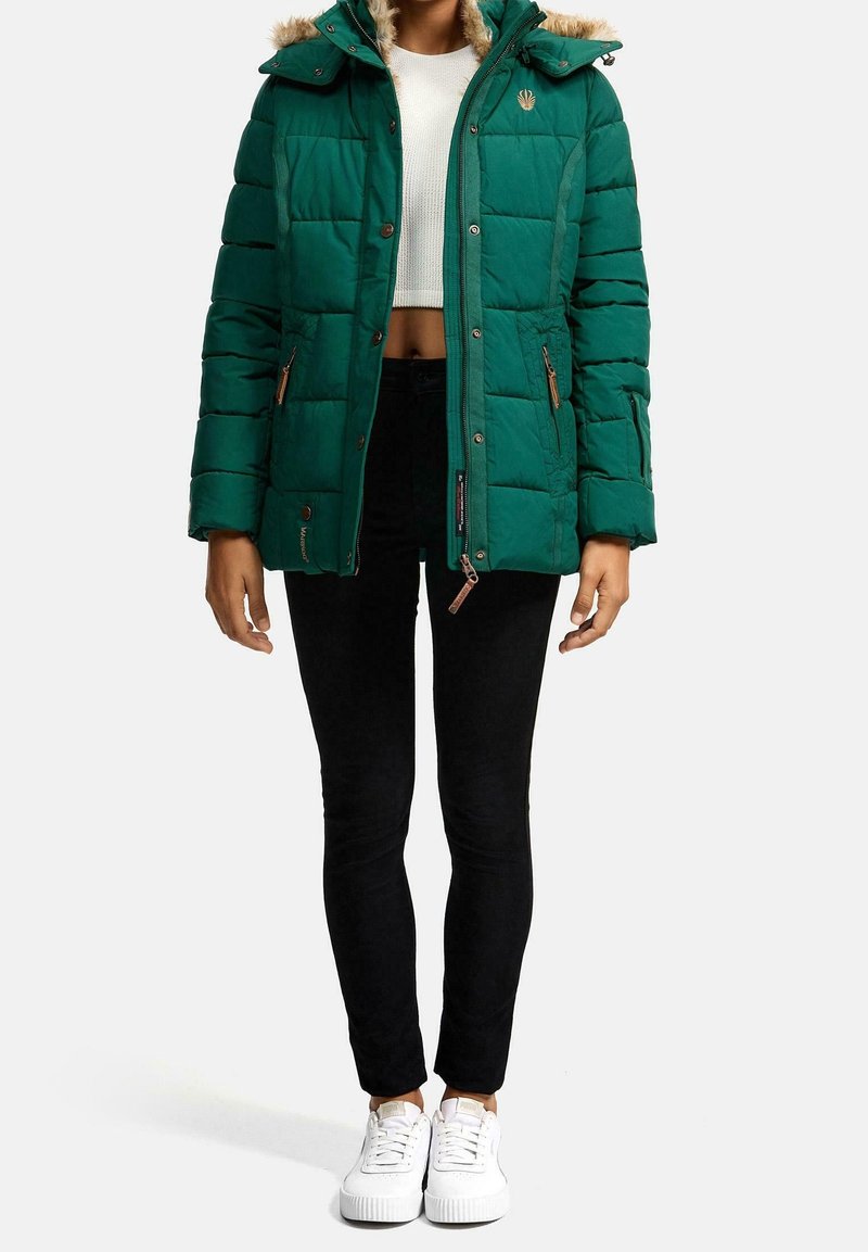 Grön puffjacka med huva i päls, vertikalt quiltad design och fickor med dragkedja. Kombinerad med svarta byxor och vita sneakers.