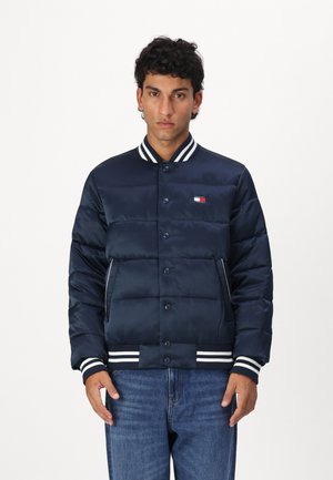 Chaqueta acolchada de color marino con cierre de botones a presión, cuello y puños acanalados a rayas, que presenta bolsillos laterales y un pequeño detalle de logo.