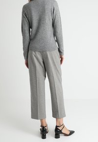 Personne portant un pull gris à manches longues, un pantalon large et court à carreaux noir et blanc, et des chaussures à talons bas noires à bride à la cheville, debout.