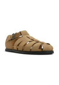 Tan suede-sandaalit, jossa on useita leikattuja hihnoja, säädettävä solkilukko ja matala musta pohja. Avoin muotoilu mahdollistaa ilmanvaihdon.