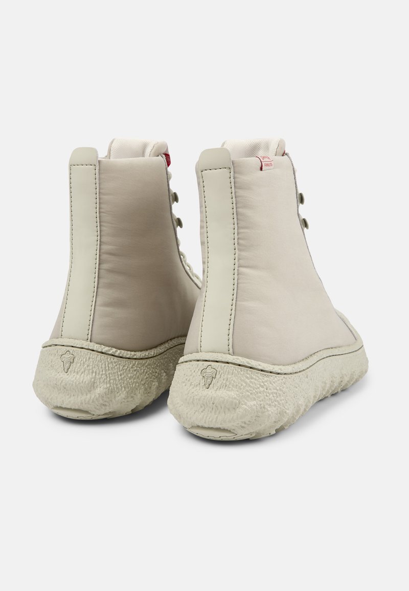 Botas de tobillo beige con parte superior de cuero suave, suela de fibra natural texturizada y acento rojo cerca de la parte superior. Detalles de costura a lo largo de los bordes.