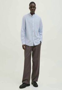 Light blue button-up shirt with a mandarin collar, paired with loose-fitting brown trousers and black shoes. Smooth fabric and relaxed fit.