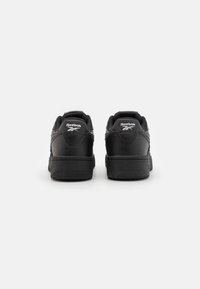 Black leather sneakers with a low-top design, featuring a textured finish, padded collars, and white logo accents on the heels.