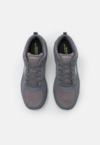 Ténis de desporto cinzentos com parte superior em malha, ponta redonda, design com atacadores, colarinho almofadado e logótipo "Skechers Memory" na língua.