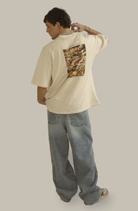 Camiseta de gran tamaño color beige con un gráfico colorido de temática alimentaria en la parte posterior, combinada con unos pantalones vaqueros de denim sueltos de color azul claro.