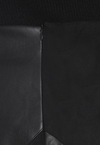 Combinaison de cuir noir et de tissu en suédine, avec une taille en tricot côtelé et un détail de fermeture éclair inséré séparant les textures.