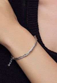 Srebrna bransoletka z skręconymi pasmami i gładkimi koralikami wzdłuż wzoru. Regulowane zapięcie łańcuszkowe z małym koralikiem akcentującym.