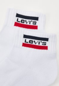 White ankle socks with a ribbed cuff, featuring a navy and red striped design and “LEVI'S” logo in black on the cuff.