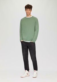 Sweater à col rond vert, manches longues, col d'accent blanc, associé à un jean foncé et des baskets montantes blanches. Design simple et décontracté.
