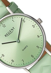 Montre à quartz ronde avec un cadran vert menthe, un boîtier métallique argenté, des index noirs et un bracelet en cuir texturé vert menthe.
